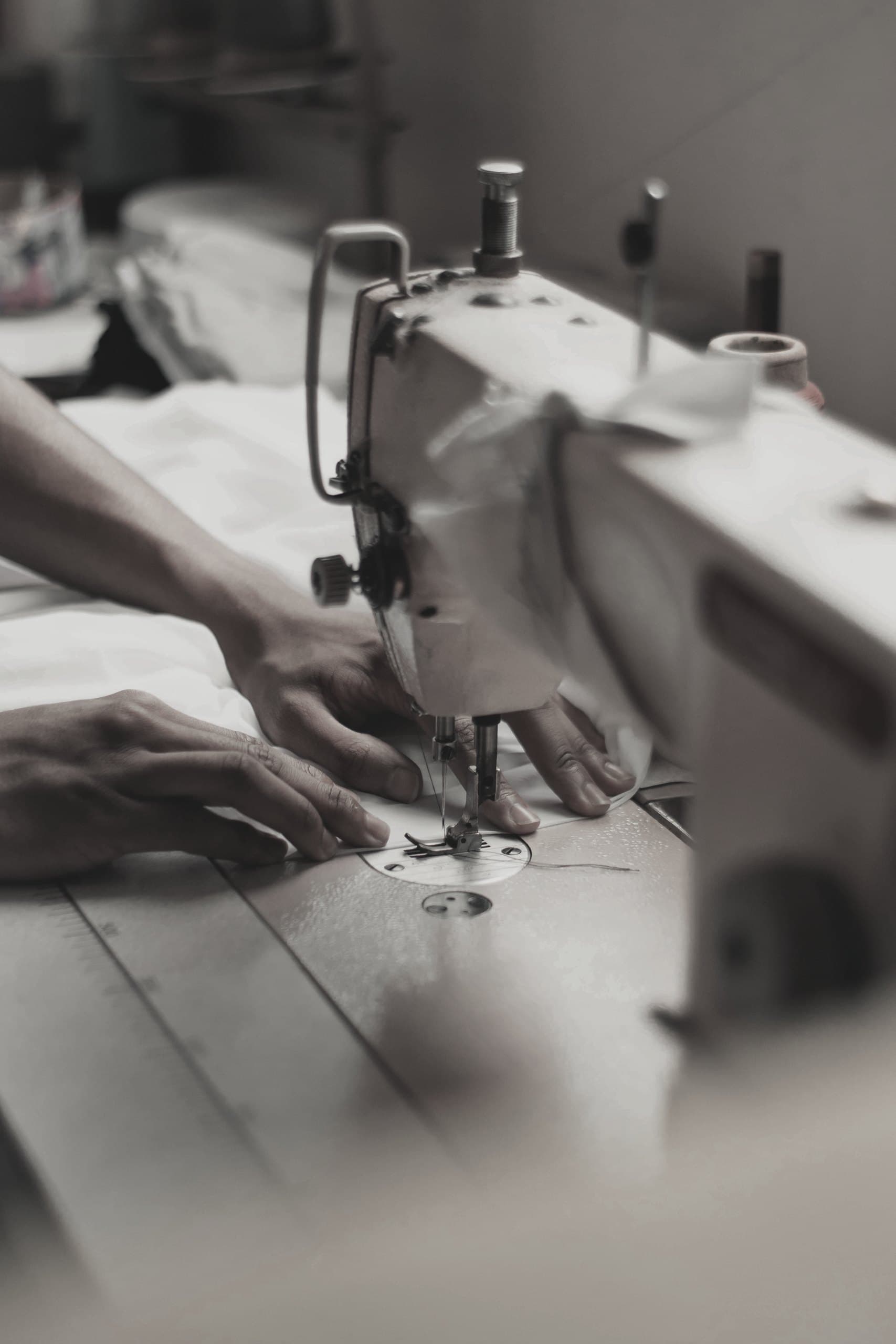 Hands guiding fabric under the needle of an industrial sewing machine.