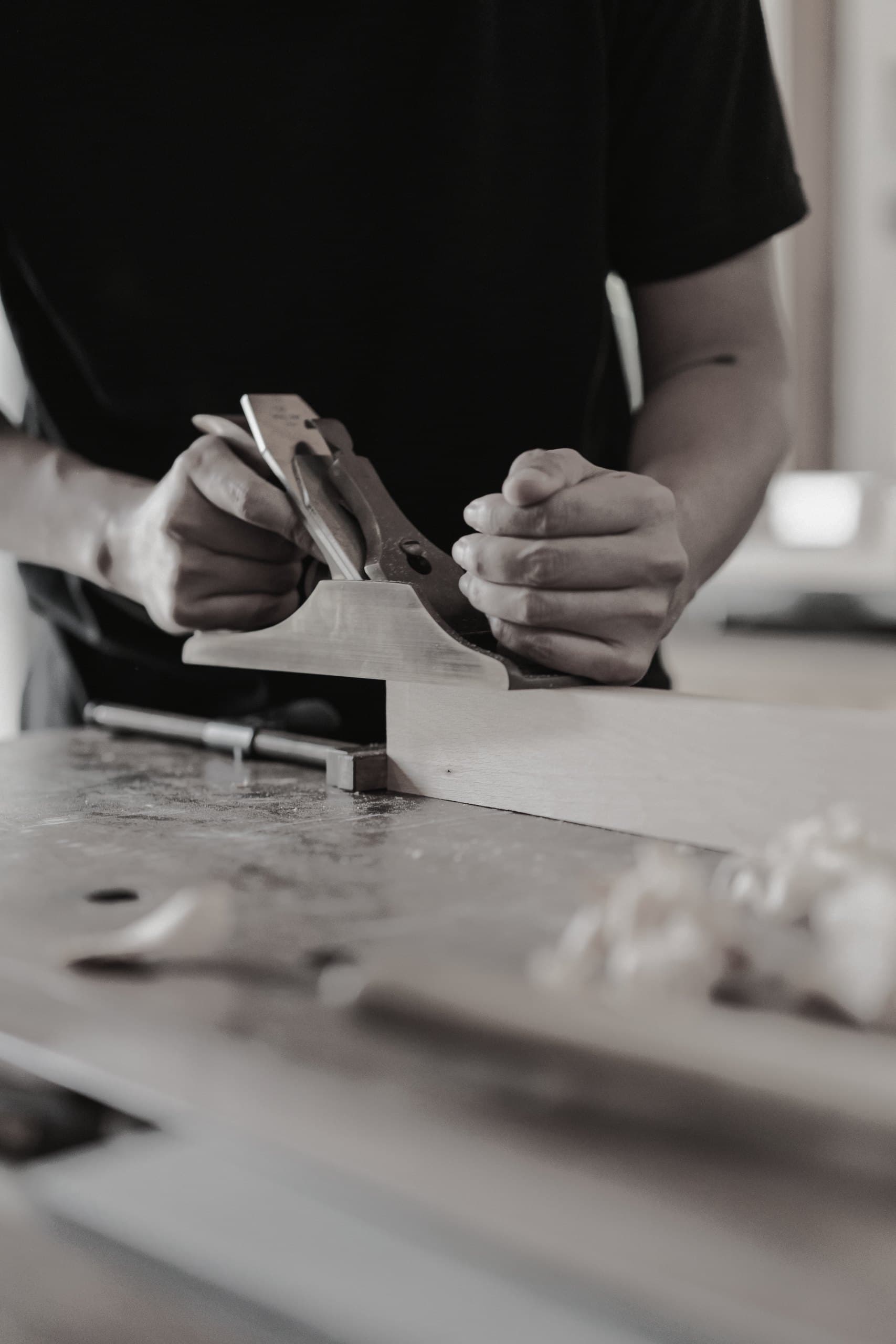 Hands carving a piece of wood with a gouge on a workbench.