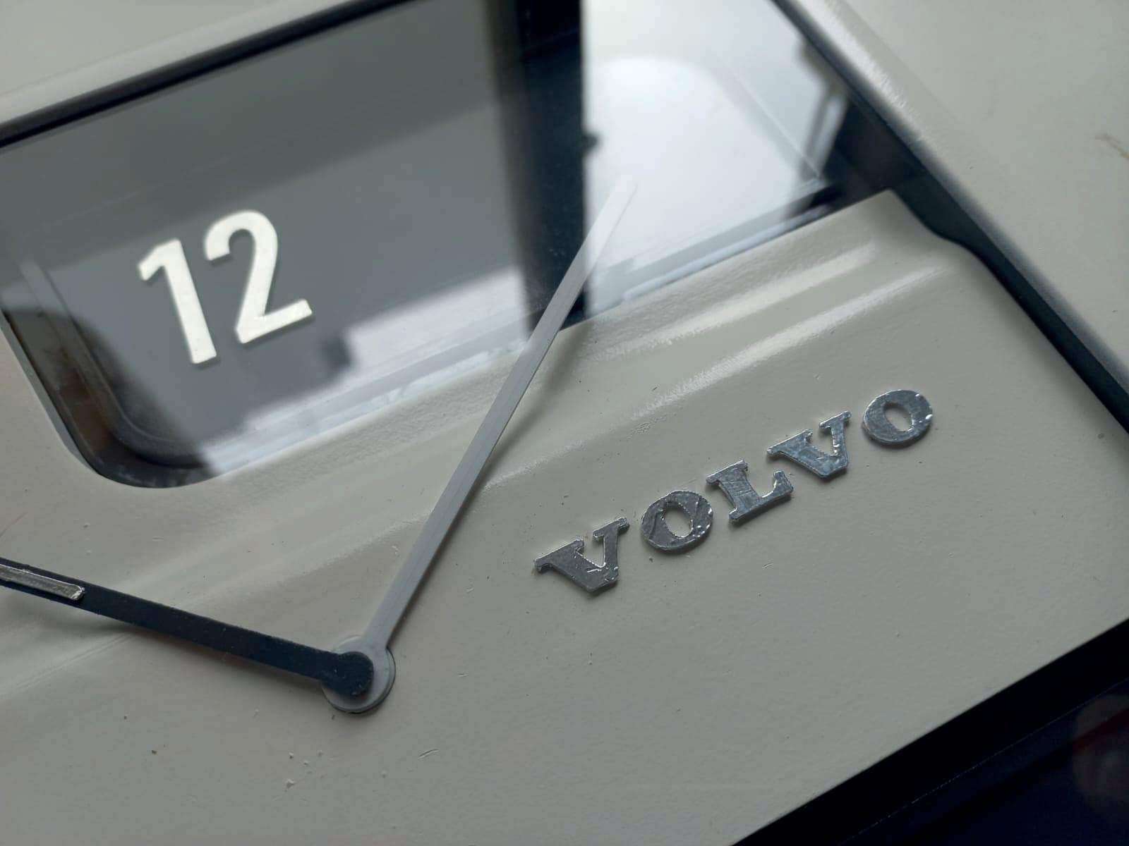 Close-up of the Volvo wordmark debossed into the clock body, with a hand sweeping over it.